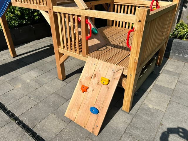 Klimwand met gekleurde klimstenen bij een houten speeltoestel